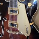 Polodupatá elektrická kytara s tmavě hnědým gradientem a černými okraji. Na zlatém plechu je nápis GRETSCH ELECTRONIC. Nástroj má dva zlaté snímače,…