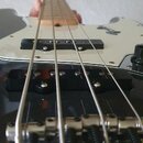 Detailní pohled na tělo a hmatník čtyřstrunné basové kytary s bílým pickguardem. Na pickguardu je čitelné logo "Squier". Nástroj má dva černé snímače…