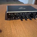 Černý zvukový interface s kovovým předním panelem. Na horní straně je logo behringer a na přední straně nápis U-PHORIA UMC204HD. Zařízení obsahuje dv…