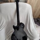 Zadní strana černé elektrické kytary s gold hardwarem. Na hlavě je viditelné logo „Epiphone“. Tělo kytary má v oblasti zadní strany lakovaný povrch s…