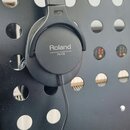 Černé monitorovací sluchátka značky Roland, model RH-5. Na vnější straně mušle je bílý nápis Roland a pod ním menší text MONITOR HEADPHONES RH-5. Slu…