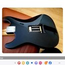 Zadní strana černé elektrické kytary s tvarem typu Stratocaster. V těle je vidět otevřený otvor s pružinami kobylníku a kovová krytka v oblasti spoje…