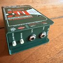 Zelená pasivní DI box s kovovým šasi. Na horní straně je nápis Radial engineering JDI PASSIVE DIRECT BOX TRANSFORMER-ISOLATED DI. Na přední straně js…