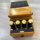 Žlutý kytarový efekt s černým ovládacím panelem a černými knoflíky se žlutými vrchy. Na horní části je nápis BOSS a text OverDrive Distortion OS-2. P…
