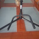 Černý kovový stojan s trojnožkou, který stojí na stole. Na horní části sloupku je viditelné malé kulaté logo s písmenem C. Povrch stojanu vykazuje mí…