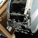 Černý buben s chromovaným obručem a ladicími šrouby. Na mechanismu pedálu je viditelný nápis SONOR. Nástroj leží na hnědé papírové krabici, na které…