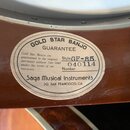 Detail ovalného štítku nalepeného na hnědém dřevěném těle banjona. Na štítku je nápis GOLD STAR BANJO GUARANTEE a text „Gold Star Banjos are guarante…