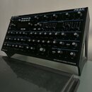 Černý syntetizátor s nápisem PEAK v pravém horním rohu a logem novation v levém horním rohu. Na spodním rámu je nápis EIGHT-VOICE POLYPHONIC SYNTHESI…