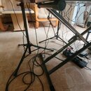 Černý klavírní stojan typu X s nápisem Soundking. Stojan drží elektronický klavír, který má v zadní části digitální displej s červeným číslem 002 a o…