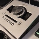 Stříbrný audio rozhraní s velkým centrálním ovládacím knoflíkem. Na horní straně je nápis apollo | twin a v dolní části logotyp UNIVERSAL AUDIO. Zaří…