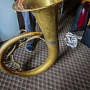 Mosazný dechový nástroj s velkým zvukovodem. Povrch je zlatavý, vykazuje známky opotřebení a drobné škrábance. Na nástroji nejsou viditelné žádné zna…