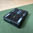 Černý DJ 컨트롤러 s modrými ovládacími prvky. Na přední straně je bílý nápis TRAKTOR s doprovodným logem. Horní panel obsahuje fader, knoflíky a tlačítka…