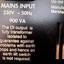 Detailní záběr na černý povrch zařízení s bílým textem. Je zde uveden nápis MAINS INPUT 230V ~ 50Hz a hodnota 900 VA. Dole je text: The DI output is…
