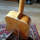 Zadní strana akustické kytary s přírodním dřevěným povrchem a bílým lemováním. Tělo nástroje vykazuje výrazné opotřebení laku v podobě rozsáhlých svě…