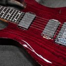 Elektrická kytara s červeným lakovaným tělem s viditnou strukturou dřeva. Nástroj má dva humbuckery a chromovaný tremolo systém. Na těle nejsou žádné…