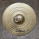 Kruhové činely z kovu s výrazným hloubením v koncentrických kruzích. V dolní části je čitelné logo Zildjian. U středu se nachází bílá nálepka s čárco…