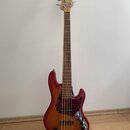 Čtyřstrunná elektrická basová kytara v červeném provedení s gradientem do žluté u okrajů. Tělo má tmavý vzorovaný pickguard a na hlavě hředu je vidit…
