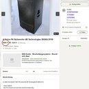 Fotografie zobrazuje černý aktivní subwoofer s hranatým tvarem a texturovaným povrchem. Na přední straně je vidět ochranná kovová mřížka a v horní čá…