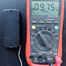 Na fotografii je červený digitální multimetr značky UNI-T, model UT61B, který ukazuje hodnotu 09.75 kΩ. Vedle přístroje je umístěn malý černý plastov…
