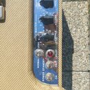 Detail ovládacího panelu kytarového zesilovače s modrým pozadím. Jsou zde vidět černé otočné knoflíky s popisky EQUALIZER, TREBLE, VOLUME a PRESENCE.…