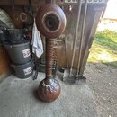 Hnědý perkusní nástroj s dvěma kulatými rezonátory spojenými válcovým trupem. Na spodním rezonátoru je vidět vyřezávaný ornament. Nástroj nemá žádné…