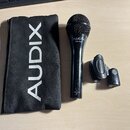 Černý dynamický mikrofon s mřížkou, na kterém je bílý nápis AUDIX a model OM-3xb. Ve spodní části těla je nápis MADE IN USA a symbol CE. Vedle mikrof…