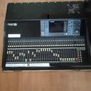 Černý digitální mixovací pult značky YAMAHA, model LS9. Zařízení obsahuje displej, ovládací tlačítka a velké množství posuvníků. Na levé straně je na…