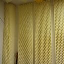 Fotografie zobrazuje akustické pěnové panely s voštinovou strukturou v krémové barvě. Panely jsou umístěny na stěnách a stropě místnosti. V levé část…