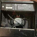Fotografie zachycuje zadní část černého kytarového komba s otevřeným krytem, v němž je vidět reproduktor a kabel. Na zadním štítku jsou uvedeny techn…