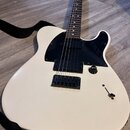 Bílá elektrická kytara s černým plechtem a hnědým hmatníkem. Na hlavě je viditelné logo "Squier". Kytara má jeden snímač u mostu, jeden ovládací knof…