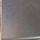 Fotografie zachycuje detail černé, texturované povrchové vrstvy obalu nebo kufru. Na povrchu jsou viditelné jemné škrábance a drobné nečistoty. Žádné…