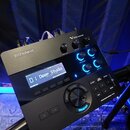 Černý elektronický bicí modul s nápisy Roland a V-Drums. Displej zobrazuje text 01 Deep Studio oraz Harp and Close. Na panelu jsou umístěny ovládací…