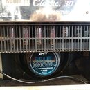 Kytarový zesilovač s nápisem Classic 30 a viditelnými elektronkami za kovovou mřížkou. V dolní části je vidět reproduktor s modrým štítkem, na kterém…