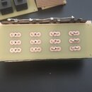 Fotografie zobrazuje dvě elektronické desky s komponenty. Přední deska je béžová a obsahuje 12 měděných kontaktních ploch uspořádaných do čtyř sloupc…