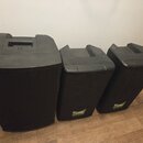 Tři černé plastové reproduktory různých velikostí umístěné vedle sebe na dřevěné podlaze. Střední a pravý reproduktor mají v dolní části zelené štítk…