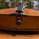 Fotografie zachycuje detail spodní části smyčkového nástroje, pravděpodobně violoncella nebo kontrabasu, v hnědém dřevěném provedení. V dolní části j…