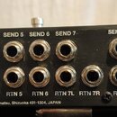 Detail zadní strany černého elektronického zařízení s řadou kovových konektorů. Nad konektory jsou bílé nápisy: IN 1, SEND 1, SEND 2, SEND 3, SEND 4,…