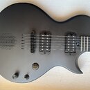 Černá elektrická kytara s matným povrchem. Nástroj má dva humbuckery, jeden ovládací knoflík a jeden přepínač. V horní části těla je integrovaný mříž…