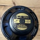 Černý reproduktor s kovovým rámem, položený na dřevěném povrchu. Na zlaté štítku je uveden nápis SPECIALLY DESIGNED FOR Fender MUSICAL INSTRUMENTS CO…