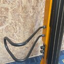 Detail žlutého nástroje s černým hmatníkem a čtyřmi strunami. Na těle je připevněna černá kovová opěrka v podobě zakřiveného trubkového držáku. V dol…