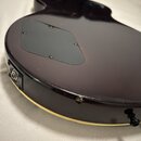 Zadní strana elektrické kytary v tmavě hnědé barvě s krémovým bokem. Na zadní straně je černý plastový kryt elektroniky připevněný čtyřmi šrouby. Na…
