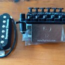 Na fotografii jsou dvě části kytarového příslušenství: černý humbucker a černý kobylník. Na snímači je bílý nápis Seymour Duncan. Kobylník má na kovo…