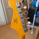 Zadní strana žluté kytarové hlavy s chromovanými ladičkami. Na dřevě je černý nápis: Designed soul focused by Fender® / 4/ ICS20009004 / Colette in I…