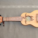 Dřevěný ukulele s přirozenou barvou laku. Na hlavě je nápis Keiki® a na těle u otvoru je stejný nápis Keiki® doprovázený vyřezáváním ve tvaru želvy.…