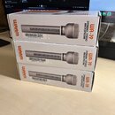 Tři identické bílé krabice s obrázkem šedého mikrofonu. Na každé krabici je oranžové logo Warm Audio a nápis WA-19 DYNAMIC STUDIO MICROPHONE. Pod obr…