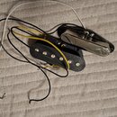 Dvě kytarové snímače s připojenými vodiči v barvách černé, žluté a bílé. Jeden snímač je typu humbucker s černým plastovým krytem a viditelnými kovov…