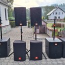Sada černých reproduktorů JBL, zahrnující dva horní reproduktory na stojanech a čtyři subwoofery v černých textilních krytech. Na každém z reprodukto…