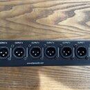 Černý rackový přístroj s řadou sedmi výstupů typu XLR. Nad konektory jsou bílé nápisy OUTPUT 7 až OUTPUT 1 a vpravo svisle ROTATABLE RACK EAR. Ve spo…
