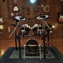 Elektronická bicí souprava značky Roland, konkrétně řada V-Drums. Sestava obsahuje dva tommy, dva činely a basový buben s nápisem Roland. Vše je umís…