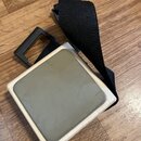 Kvadranový cajon v přírodním dřevě s šedou dopelnivou deskou na horní straně. K nástroji je přiložen černý textilní popruh s plastovou sponou. Povrch…